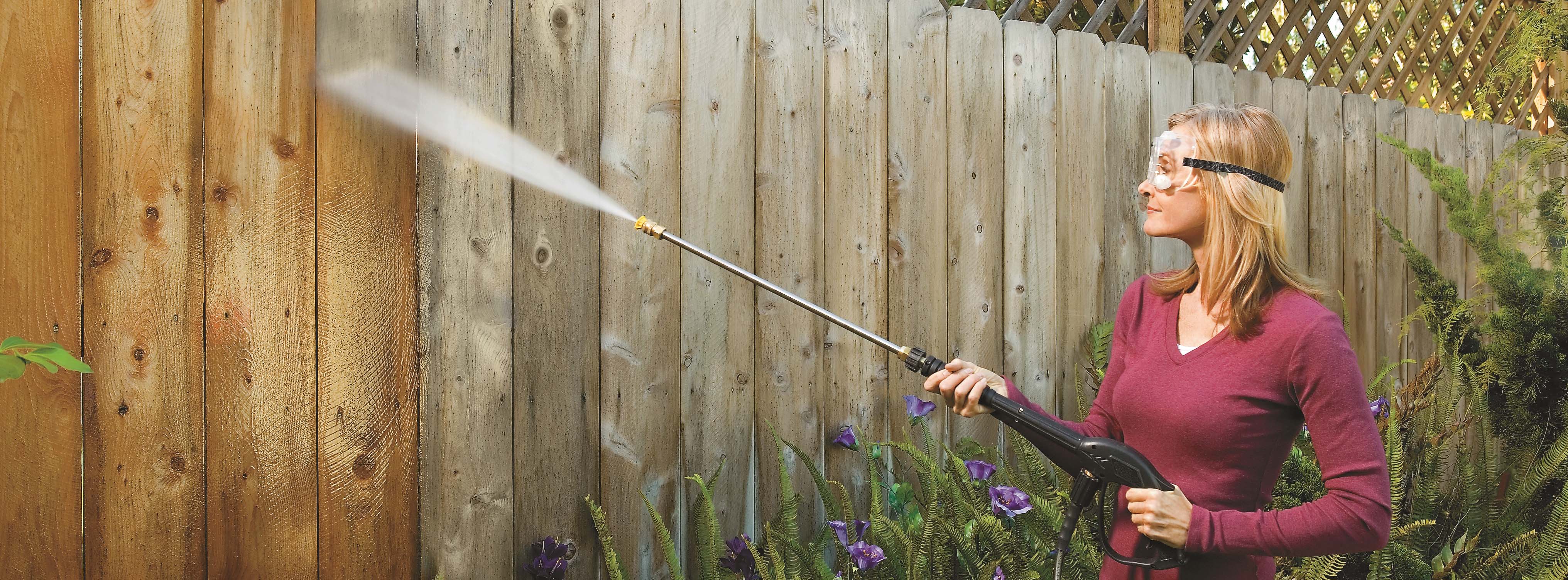 Woman Cleaning Fence With Pressure Washer